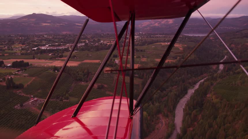 Aerial view of a river and small town from the cabin of a vintage red biplane at evening