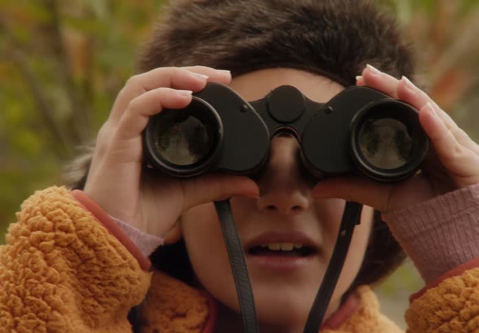 A young female kid is looking through binoculars around the forest area