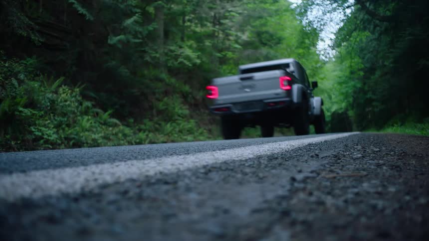 A gray truck travels on a road through the woods