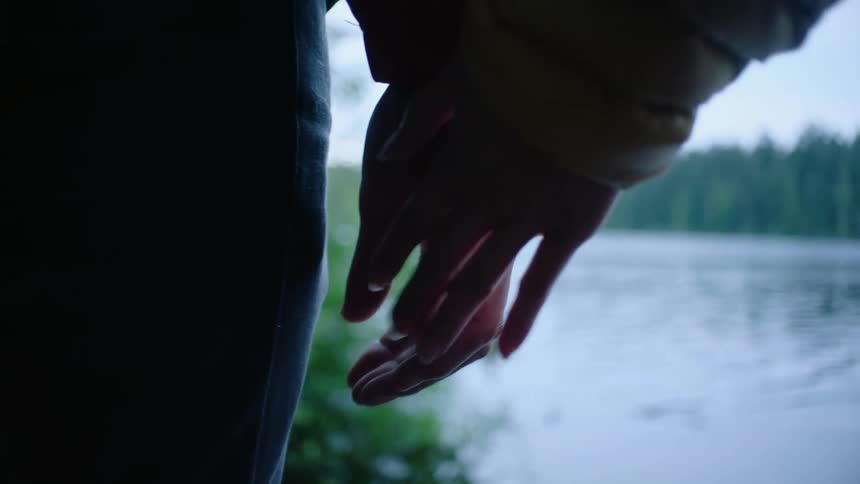 Close up of a woman taking the hand of a man standing near a river next to the forest