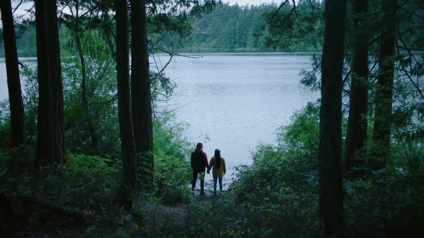 A couple is holding hands around the forest area by the lake