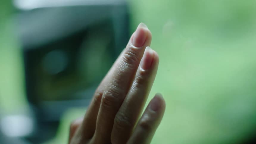 A woman gently taps her fingers on the passenger window of a vehicle that is in motion