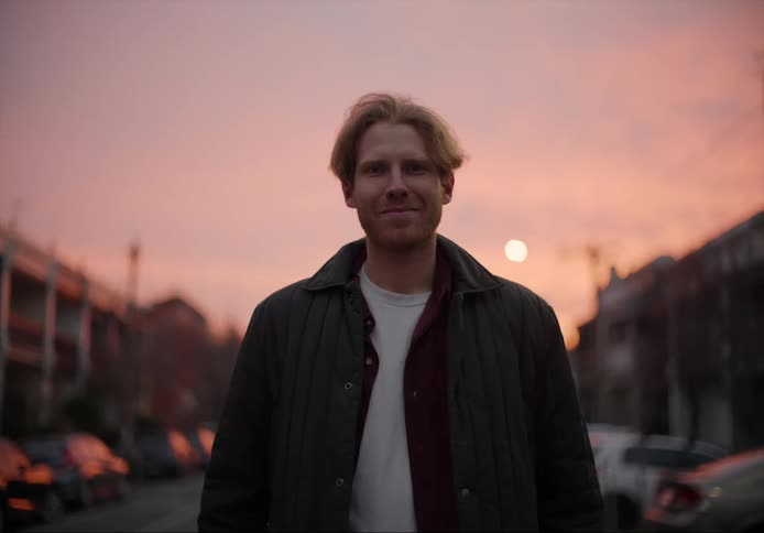 A man standing in the street of a small town looks up and smiles at sunset