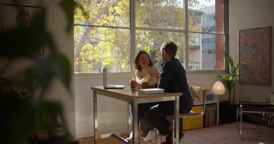Colleagues laugh while sitting at a desk together with a laptop