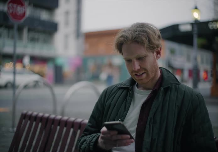 A man laughs as he scrolls through his smartphone while sitting downtown