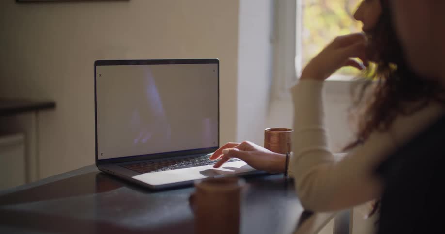 Woman sitting on a desk at home uses a laptop with a blank replaceable screen