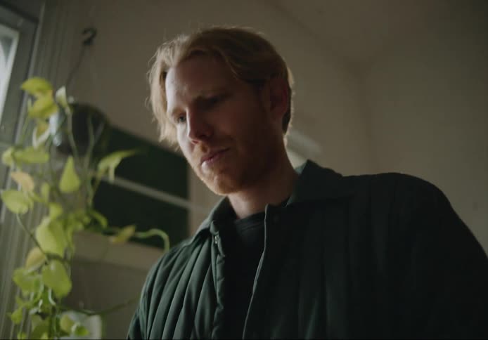 A young white man is inside of his house and is on his laptop