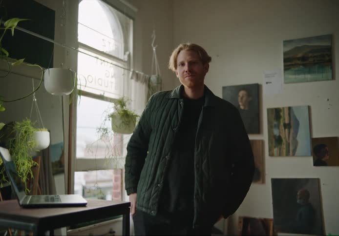 A man is standing near his laptop computer and smiling