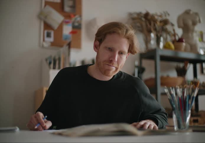 A young white man is inside of a studio and is painting