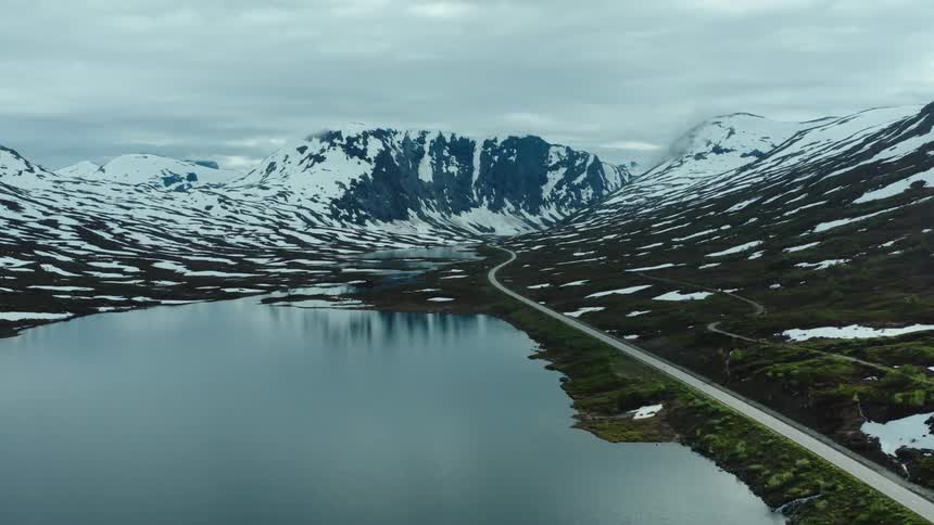A frozen lake beside a road through a snowy mountain valley on a cloudy day