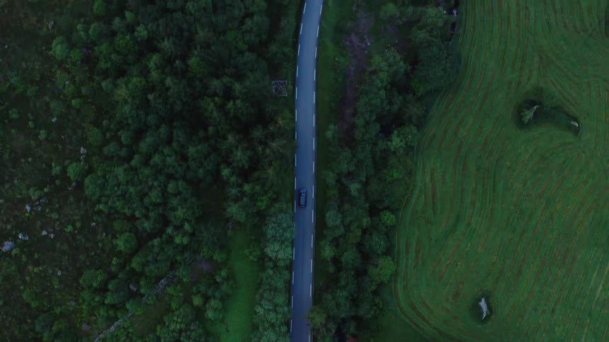Aerial view of a car driving on a rural road surrounded by crop fields and forests