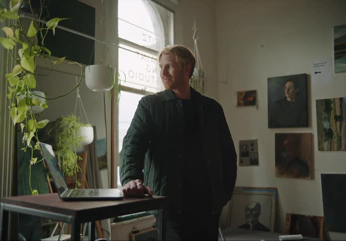 A man is standing by his laptop thats on a table