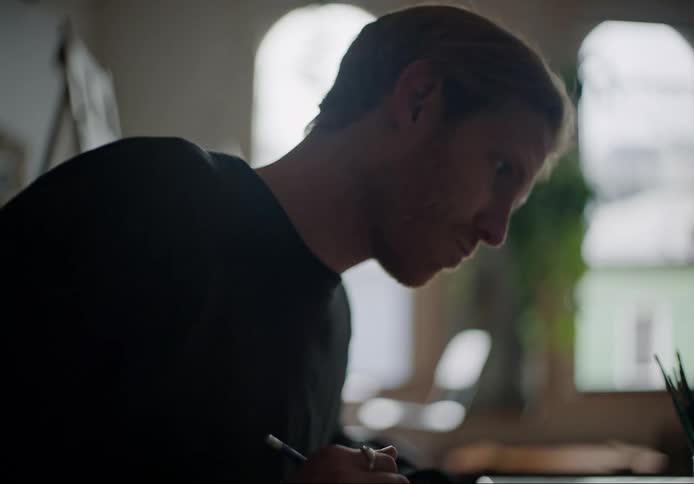Young man sitting at a desk at home drawing with a pencil on paper