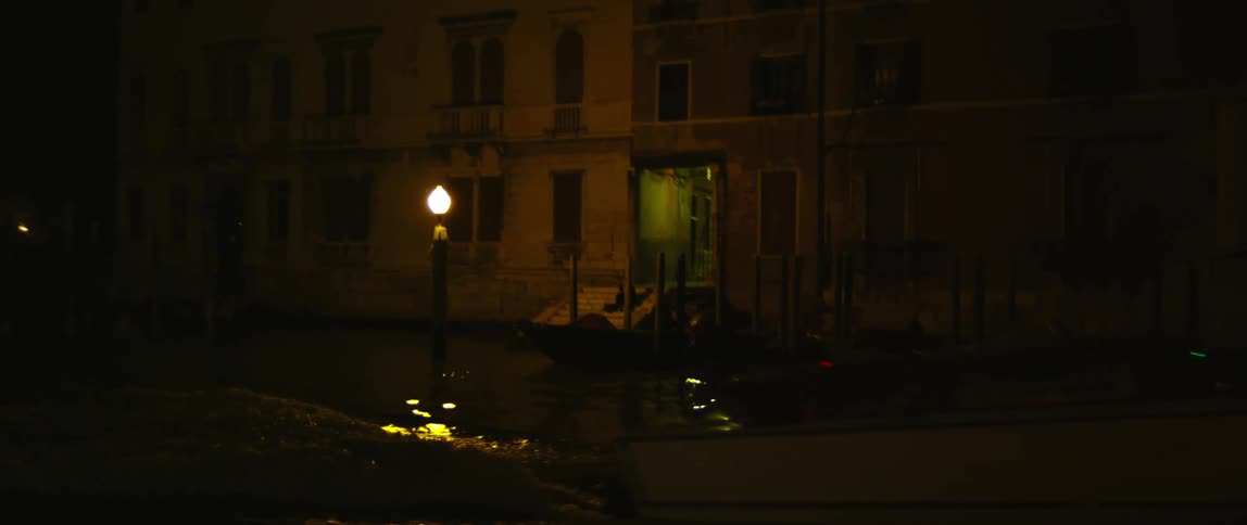 A man operates a speedboat past a neighborhood at night