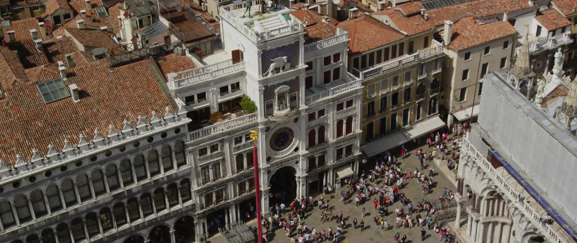 Crowd of people move along plaza near clock building