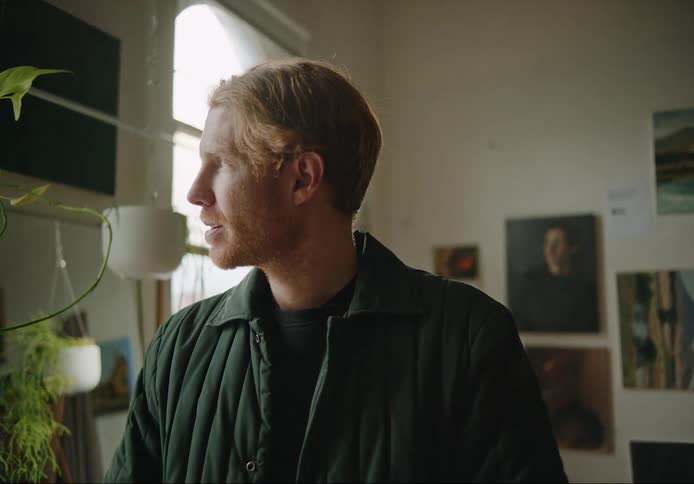 Young blonde bearded man standing in a room at home turns to look out the window