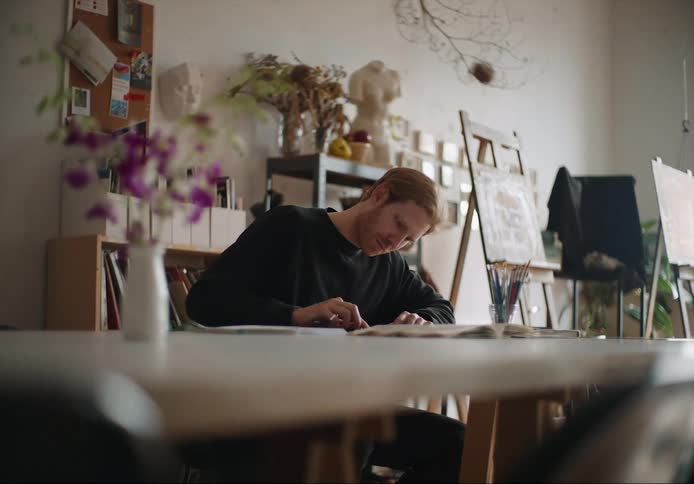 A young white man is painting a picture on his desk in the day time
