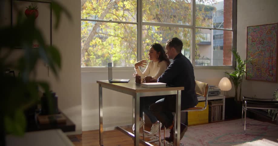 Two coworkers sit in office and discuss contents on laptop