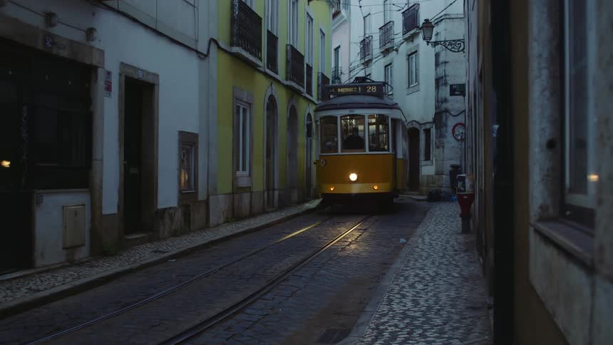 A full trolley winds through a curved road in a city with cobblestone sidewalks