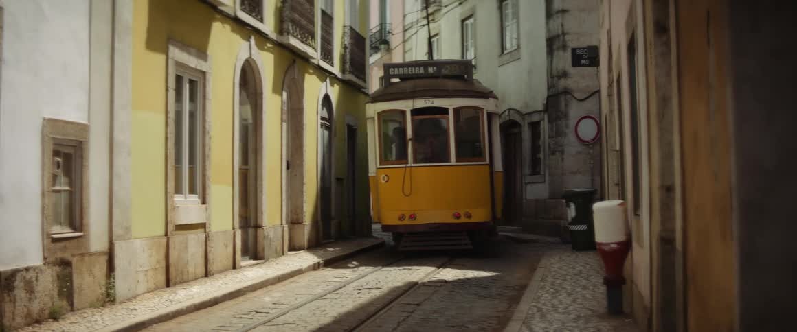 Yellow tram moving up the narrow street between houses in lisbon