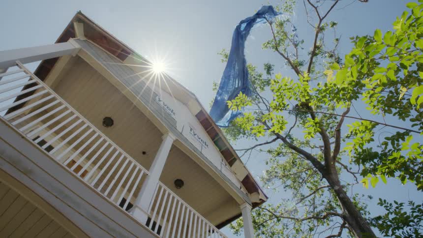 Sun peaks over roof of house shining onto blue banner tangled in tree top