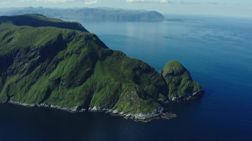 Aerial view of a promontory at the end of a mountain range next to the blue ocean water