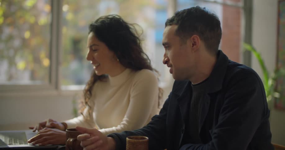 Young couple sitting at a table in the living room talk while looking at a laptop