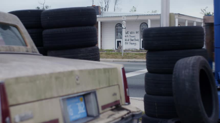 Car parked near piled up used tires in front of a house with a graffiti on the wall
