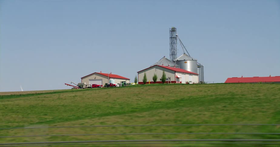 Road passes by large farm with multiple silos and buildings