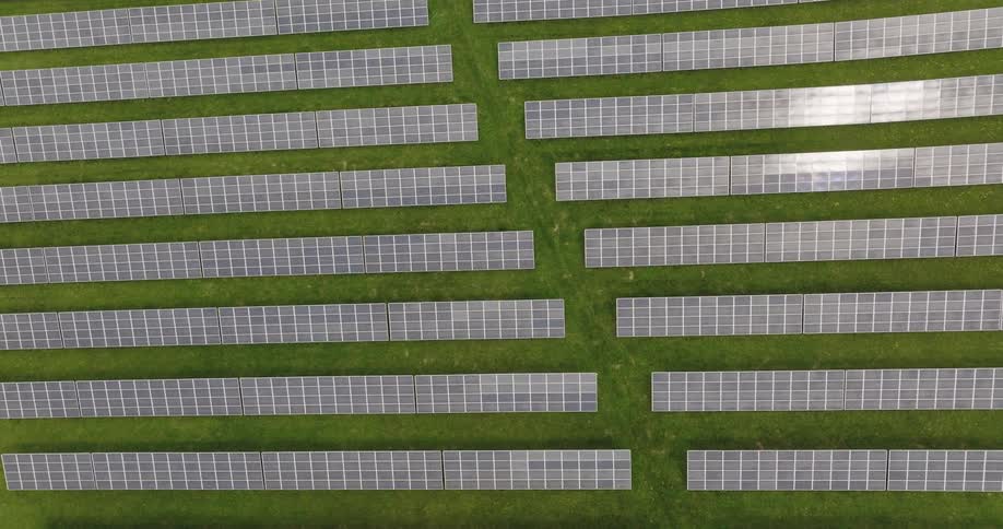 Twisting top down aerial view of rows of solar panels over the green grass of a field