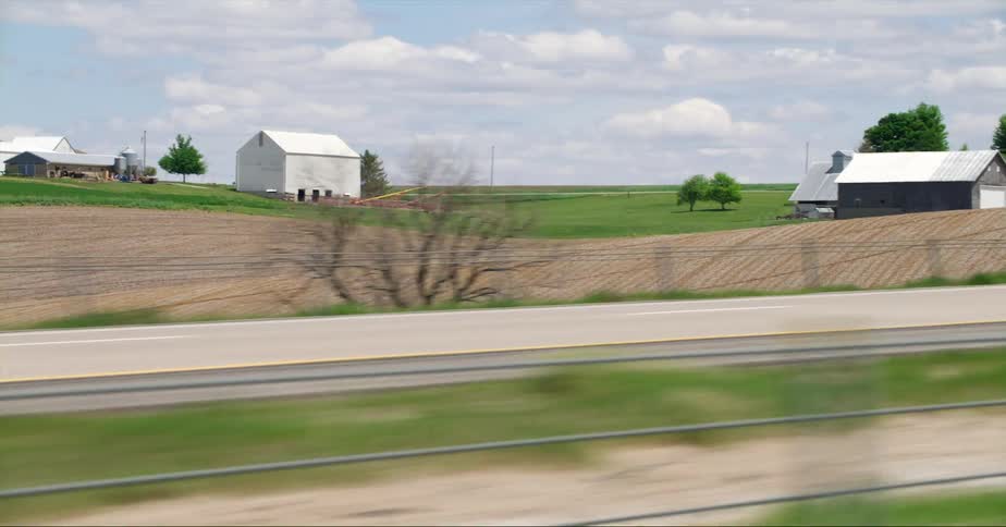 A farm with grain elevators barns and fields set back from the highway and heavy truck traffic