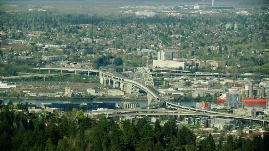 Portland city traffic crosses the I-5 bridge in the heart of the city in this late spring season aerial with PDX airport in the background
