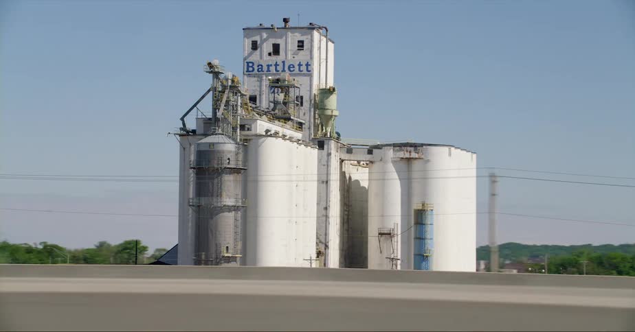 Elevator and grain silos stand next to a highway under a blue sky