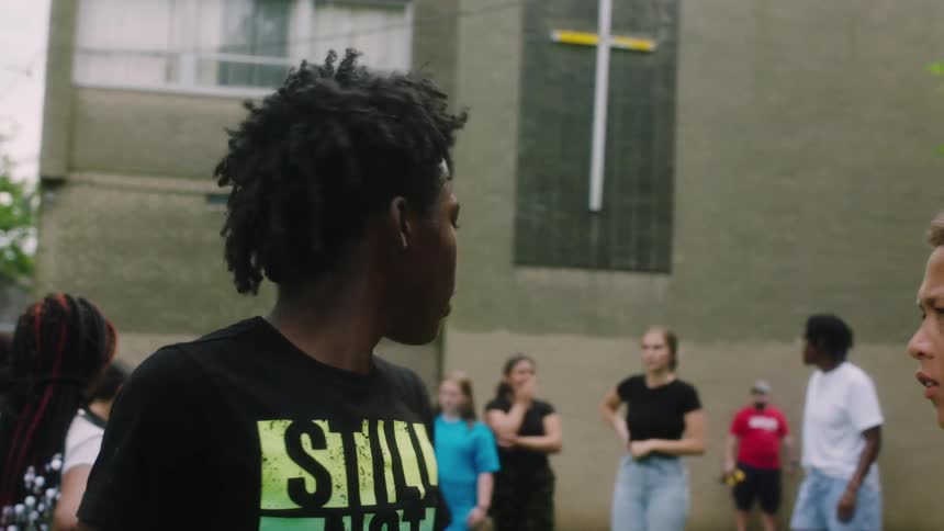 Boy picks people and gives directions while standing with others on lawn near church