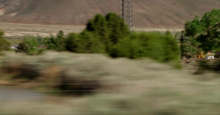Hay bales piled up on the field of a farm seen from a fast moving vehicle