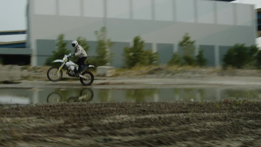 Motorcyclist pops wheelie while splashing through puddle in a lot near the overpass