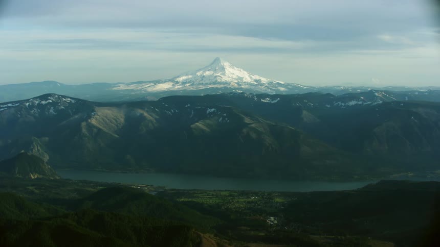 The Columbia River gorge cuts through rugged mountain terrain in this wild aerial shot with Mount Hood center frame as the camera flies north