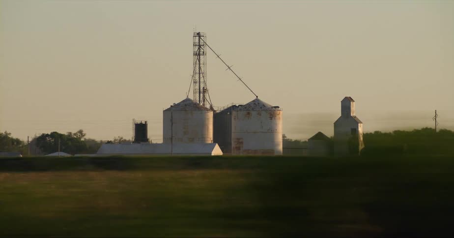 Two large grain silos sit on a farm in the middle of a field