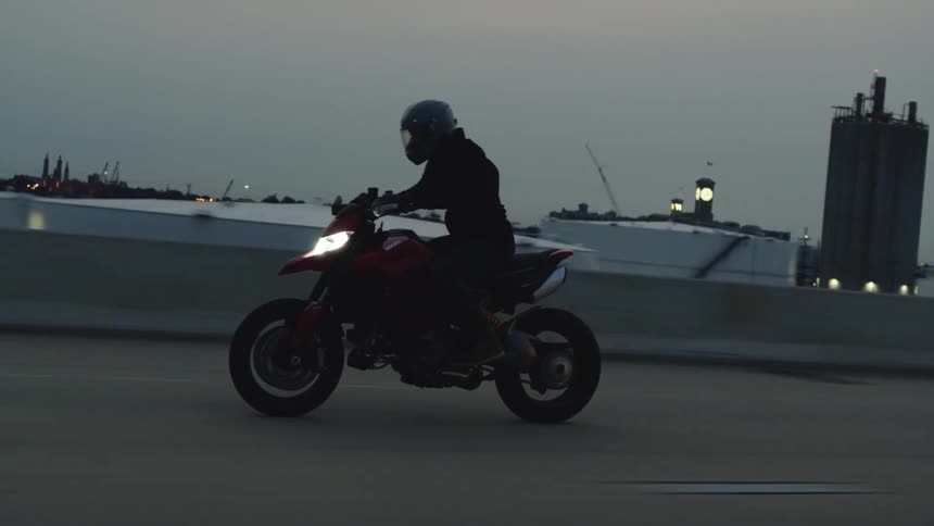A person wearing protective helmet and clothing is riding on a motorcycle down a industrial building lined freeway