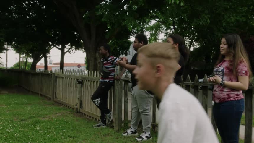 Boy claps and jumps as he and others stand near fence watching activity