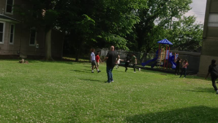 Family and friends playing a casual game of soccer over the green grass in the backyard at home