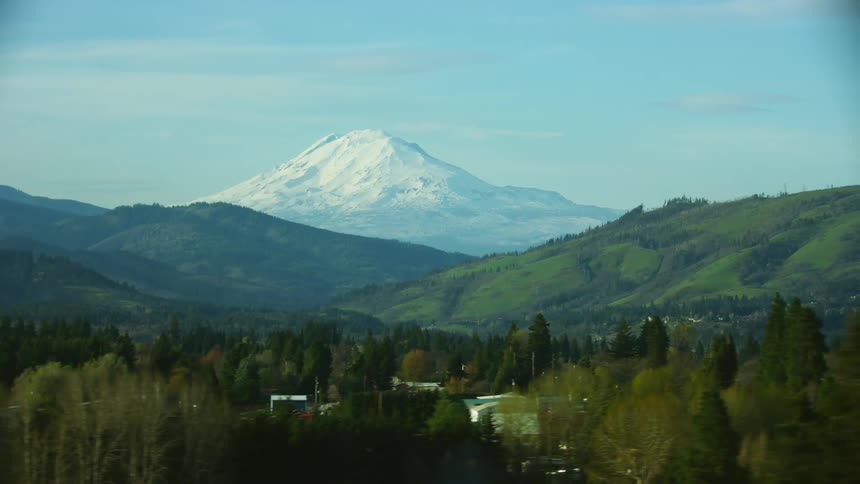 Trees and buildings in a valley with a snow covered mountain in the distance