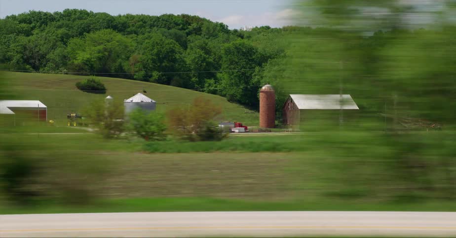 Barns and silos on a field in a farm close to a road seen from a moving vehicle at daytime