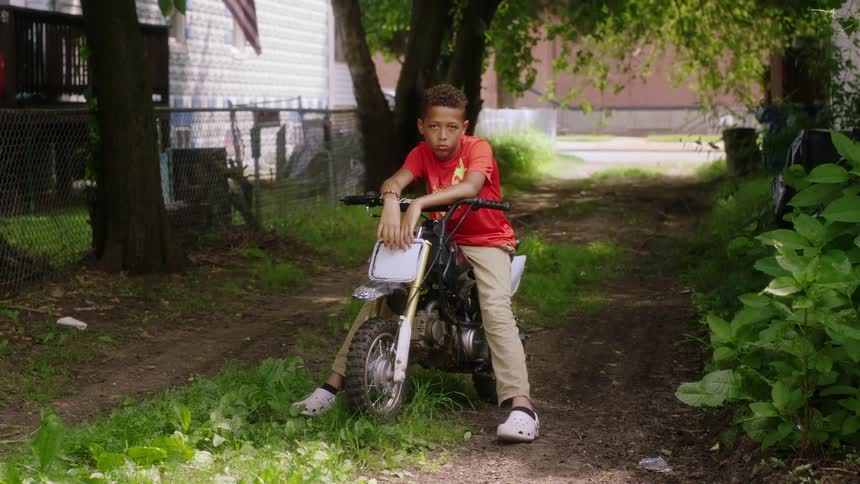A child is sitting on a bike near his house