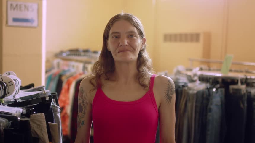 A woman is standing in a store near clothes racks smiling