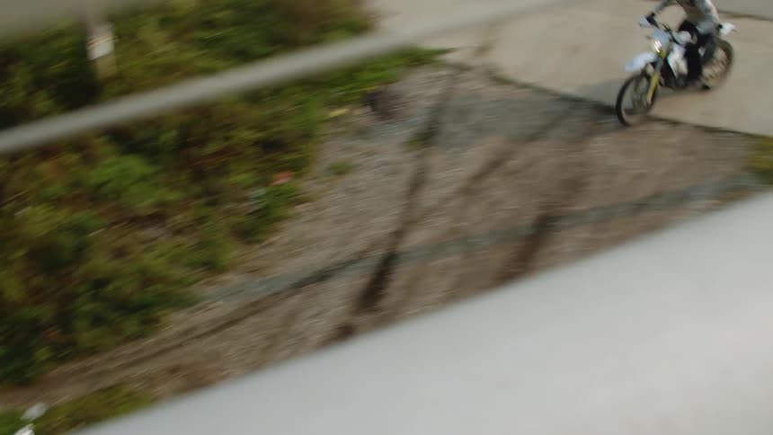 A motorcyclist wearing a light colored helmet and a jacket is riding through the bike path among the bushes
