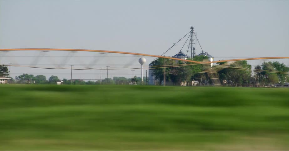 Vehicles flow along highway past commercial farms with several silos