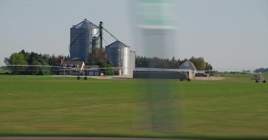 Trucks and cars are driving on ahighway near a farm