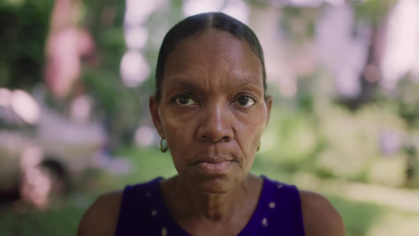 A black woman in a neighborhood lifts her head and stares with determination