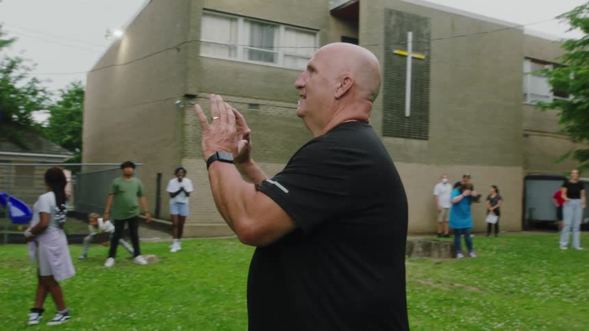 Older man catches ball as he stands outside church with youths